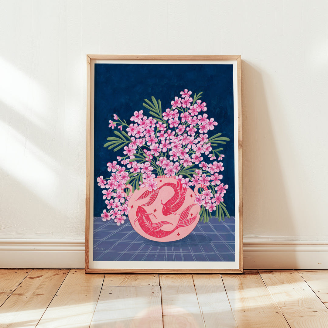 Framed artwork with pink floral design on a blue background, placed on a wooden floor.